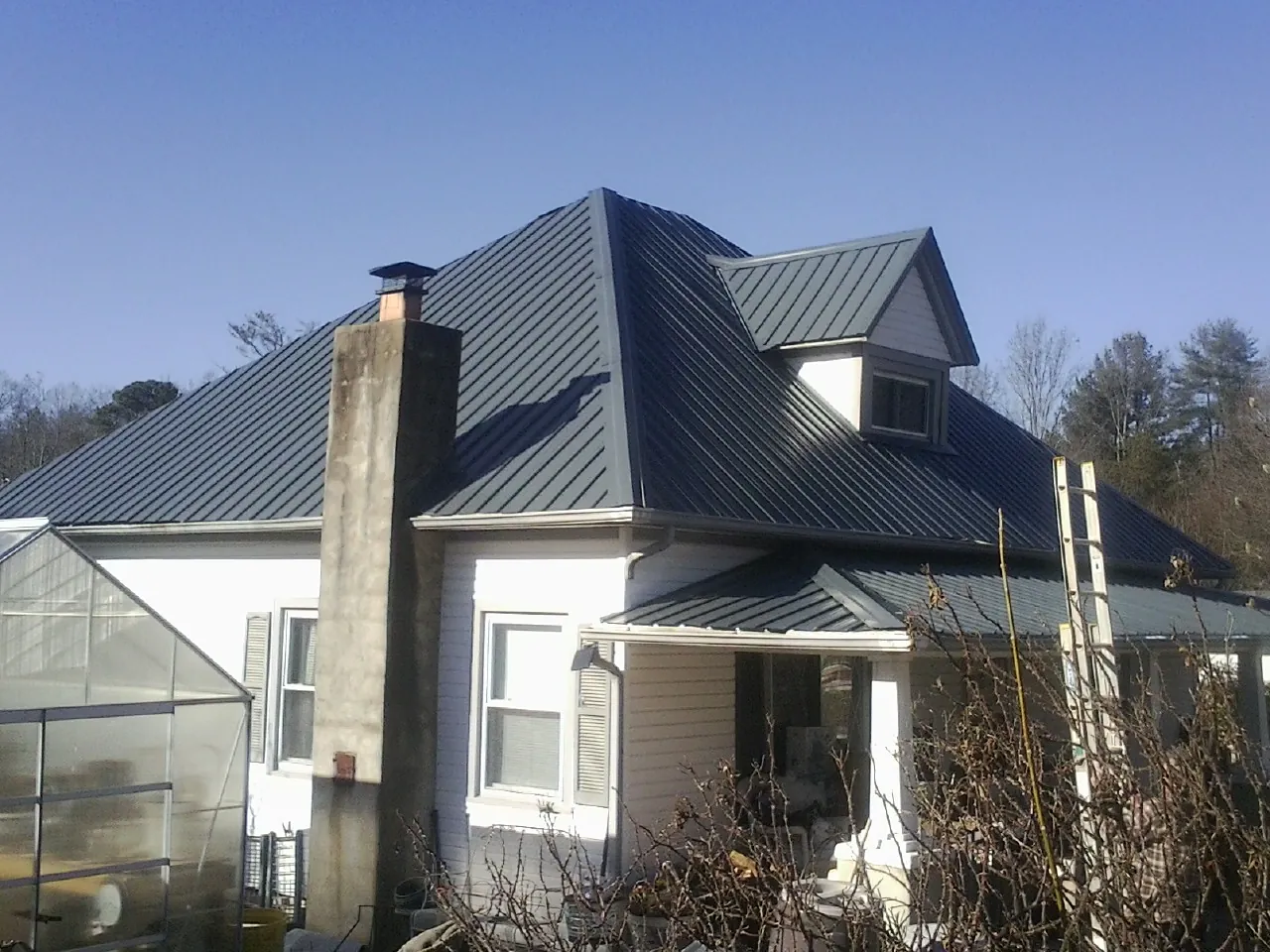 Dark blue standing seam metal roof on a white farmhouse with dormer — Slate & Tile Roof Repair by Roofing Brothers in Randlett