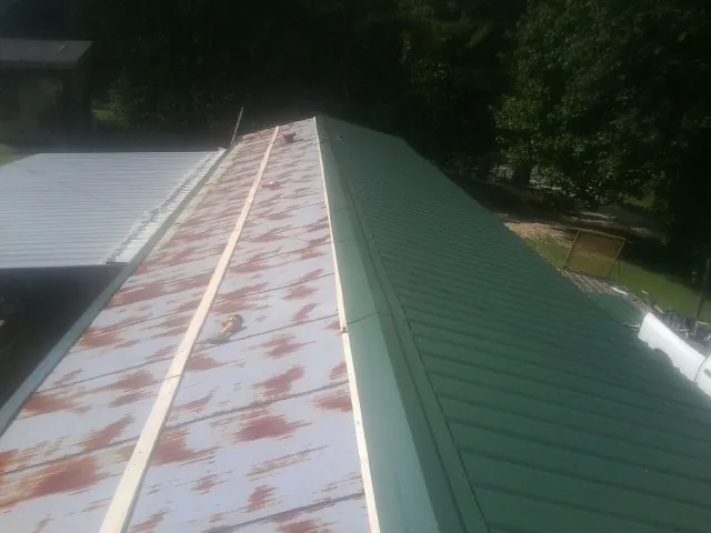 Old rusted panels beside newly installed green metal roofing — Wind Damage Roof Repair by Roofing Brothers in Randlett