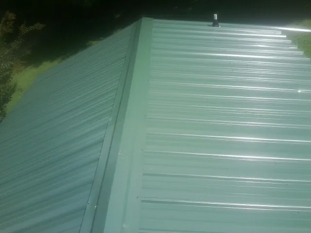 New green metal panels meeting at the ridge of a roof — Flat Roof Repair work by our crew in Randlett